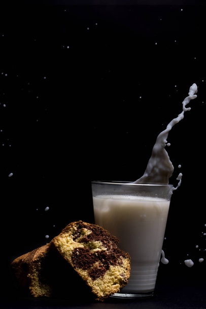 Milk glass splash with cake dessert isolated on black background - Photo, Image