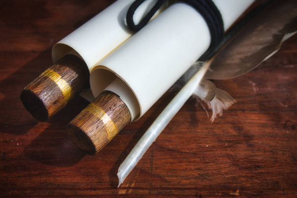 Close-up of old-fashioned paper scroll with a feather quill pen on a wooden table - Photo, Image