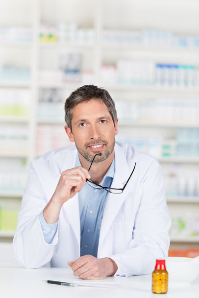 Male Pharmacist Holding Glasses At Pharmacy Counter - Foto, Imagen