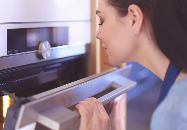 Beautiful young woman checking how her cake is doing in the oven - Foto, Imagem