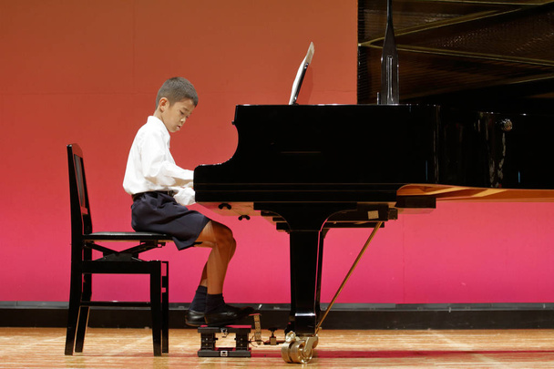 Játék a japán fiú zongorán játszik a színpadon (negyedik fokozat az elemi iskolában) - Fotó, kép