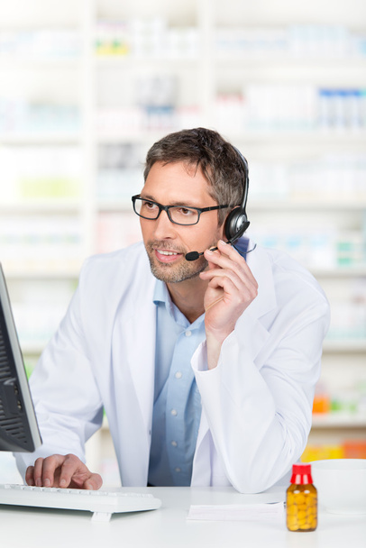 Pharmacist Wearing Headset While Using Computer At Counter - 写真・画像
