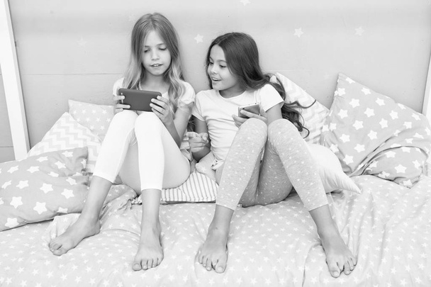 Girls sisters wear pajama busy with smartphones. Children in pajama interact with smartphones. Application for kids fun. Internet surfing and absence parental advisory. Smartphone internet access - Photo, image
