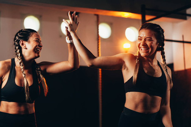 Lächelnde Frauen, die High Five im Fitnessstudio machen. Junge Frau macht High-Five-Geste im Fitnessstudio nach dem Training - Foto, Bild
