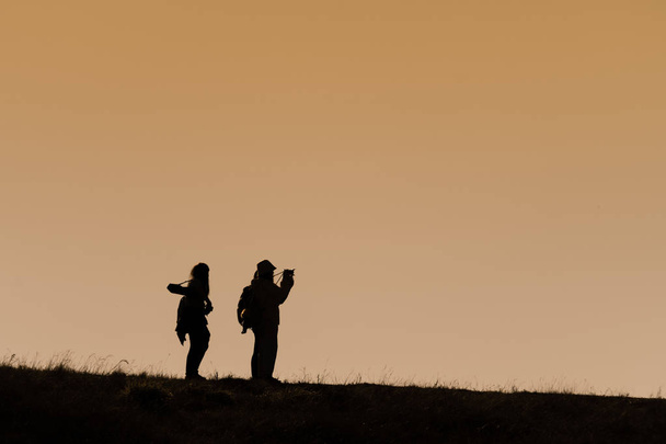 Silhuetas de caminhantes com mochilas desfrutando de vista do pôr do sol a partir de t
 - Foto, Imagem