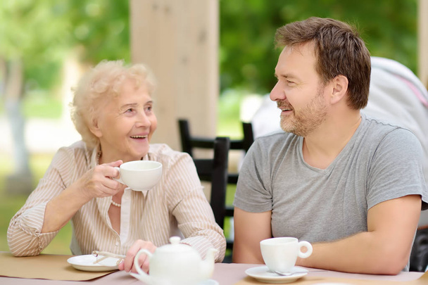 Beautiful senior lady with his mature son drinking tea in outdoors cafe or restaurant. Elderly lady lifestyle. - Φωτογραφία, εικόνα