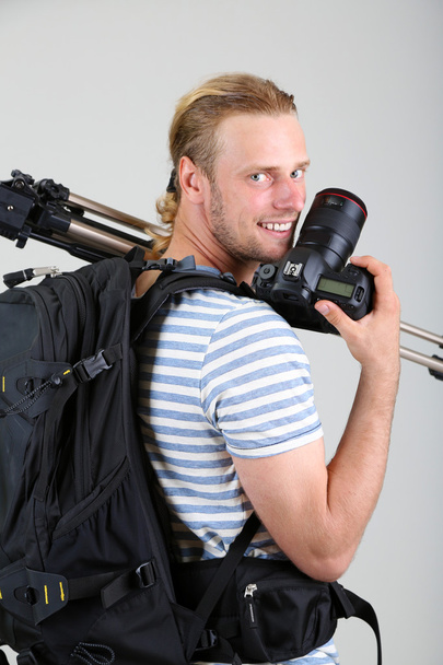 Portrait of handsome photographer with camera and tripod, on gray background - Fotografie, Obrázek