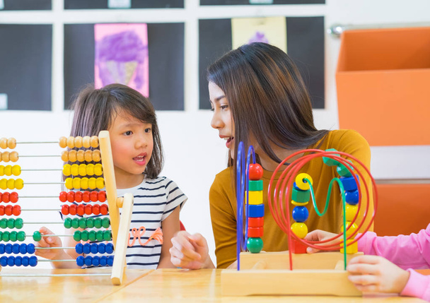 Asian female teacher teaching mixed race kids play toy in classr - Фото, изображение