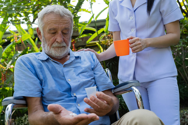 senior man sitting on wheelchair and eating medecine with nurse, - Photo, Image