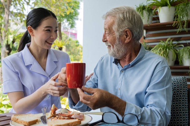 senior man happiness with smiling nurse, takes care breakfast at - Photo, Image