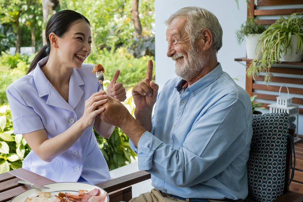 senior man happiness with smiling nurse, takes care breakfast at - Photo, Image