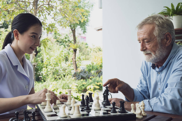ανώτερος άνθρωπος ευτυχία και νοσοκόμα, παίζοντας σκάκι στο μπαλκόνι κοντά GA - Φωτογραφία, εικόνα