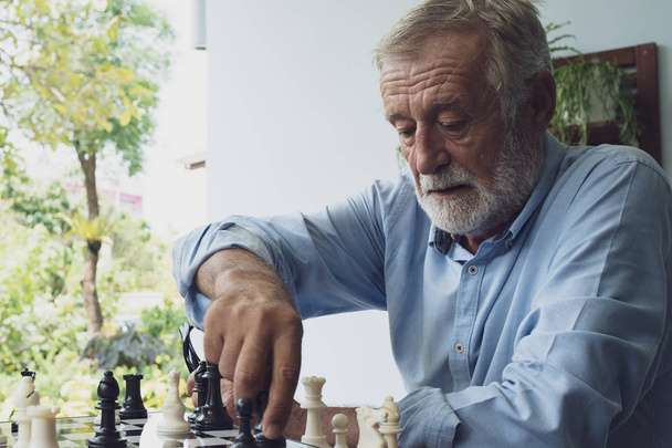 ανώτερος άνθρωπος παίζοντας σκάκι στο μπαλκόνι κοντά στον κήπο στο γηροκομείο  - Φωτογραφία, εικόνα