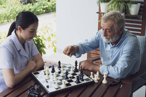 starszy mężczyzna szczęścia i pielęgniarki, grając w szachy na balkonie w pobliżu ga - Zdjęcie, obraz