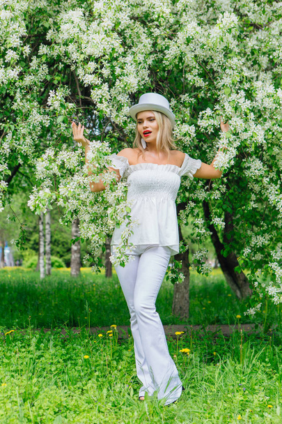 Sexy modern bride in white cylinder hat enjoing blooming apple tree flowers. - Fotó, kép