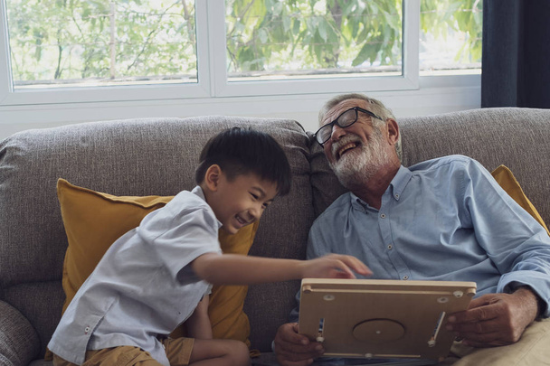 vanhempi mies onnellisuus ja pojanpoika istuvat sohvalla ja pl
 - Valokuva, kuva