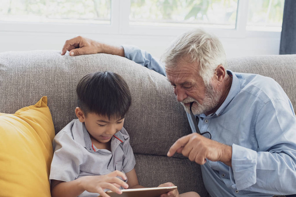 Starší člověk štěstí a vnuk sedí na pohovce a pl - Fotografie, Obrázek