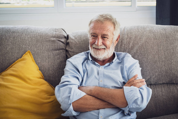 vanhempi mies onni istuu sohvalla ja hymyilee ja peukalot
  - Valokuva, kuva