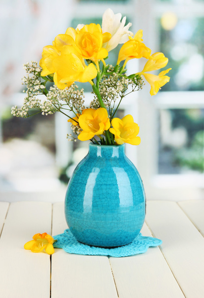 Beautiful bouquet of freesia in blue vase on wooden table on window background - Zdjęcie, obraz
