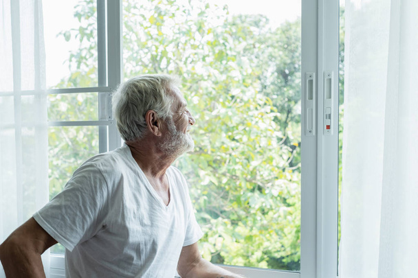 старший человек думает и смотрит в окно в белой комнате
 - Фото, изображение