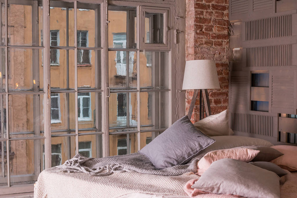 interior del apartamento loft. Interior minimalista con cama de madera simple, lámpara, ropa de cama blanca. Colores pastel, gran ventana.Acogedora habitación
 - Foto, Imagen