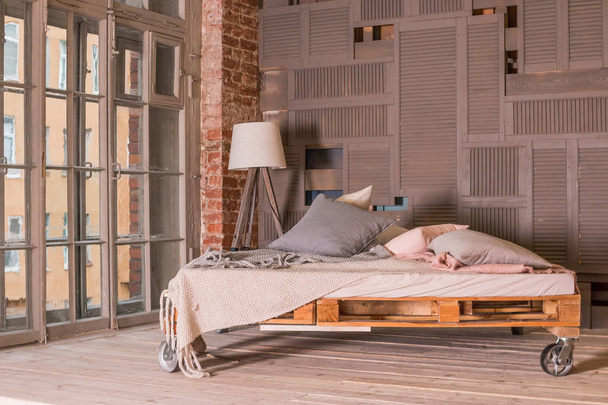 Loft lakás belső. Minimalista enteriőr egyszerű, fából készült ágy, lámpa, nagy ablak. Stílusos hálószoba loft stílusú pasztell színekkel. Lemezterület másolása - Fotó, kép