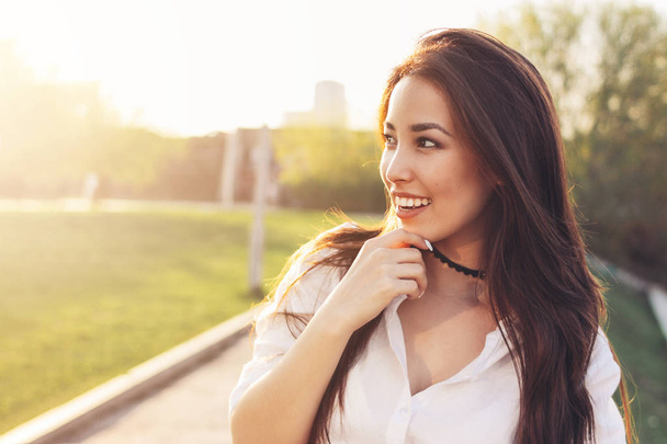 Positive beautiful happy asian girl in white shirt on city street background, summer sunset time - 写真・画像