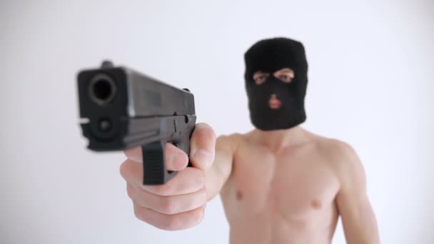 バラクラバで裸の胴子を持つテロリストは、白い背景に彼の銃を目指しています - 映像、動画