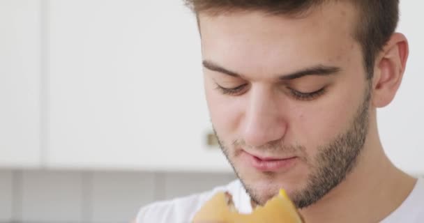 Young man is eating burger at home and talking with somebody. - Metraje, vídeo