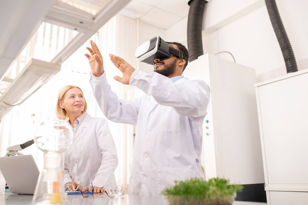 New vision of science: curious young Arabian scientist in lab coat using virtual reality simulator while watching educational video and studying genes and cells - Photo, Image