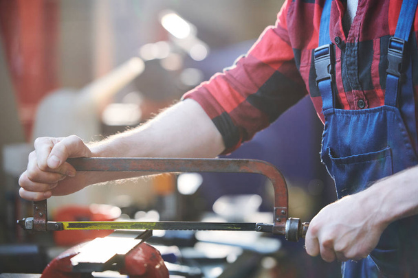 Молодой рабочий или плотник в комбинезоне и фланели с помощью ручной пилы для резки металлических деталей
 - Фото, изображение