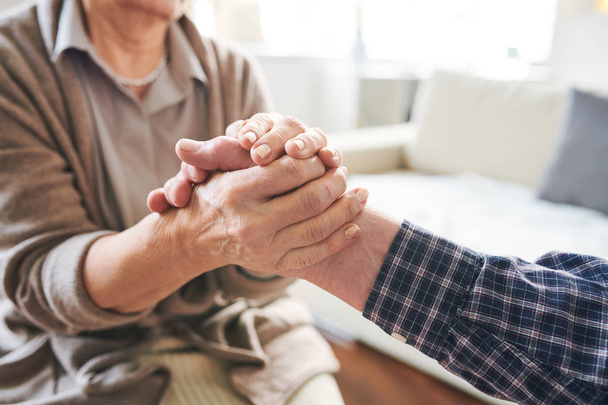Mature retired woman holding hand of her senior spouse or caregiver expressing support, affectiona and love - Photo, Image