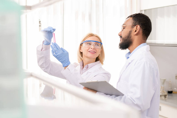 Positieve zelfverzekerde medische wetenschappers in labcoats tevreden met het resultaat van experiment onderzoek vloeistof in reageerbuis - Foto, afbeelding