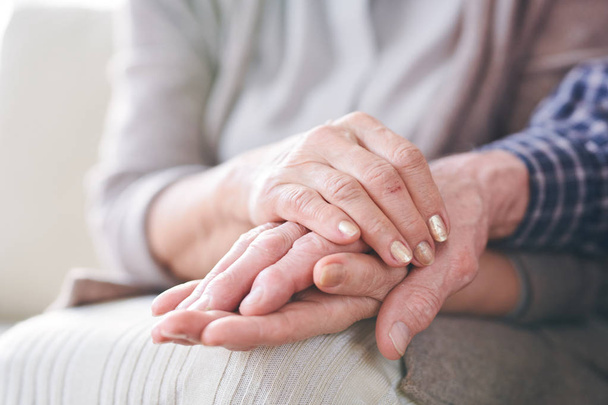 Manos de esposa madura o cuidadora que sostienen la de su esposo o paciente anciano como expresión de cuidado y apoyo
 - Foto, imagen