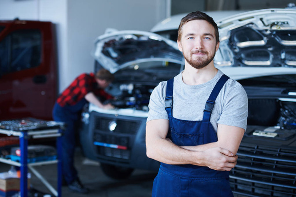 Young bearded successful repairman of car service center standing in front of camera inside workshop - Photo, Image