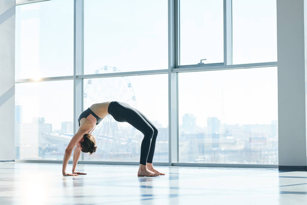 Menina magro em activewear praticar postura backbend com as mãos e os pés tocando o chão durante o treino
 - Foto, Imagem