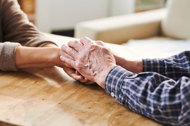 Поддерживающий старший муж, держась за руки своего престарелого супруга, выражая сочувствие, заботу и любовь
 - Фото, изображение