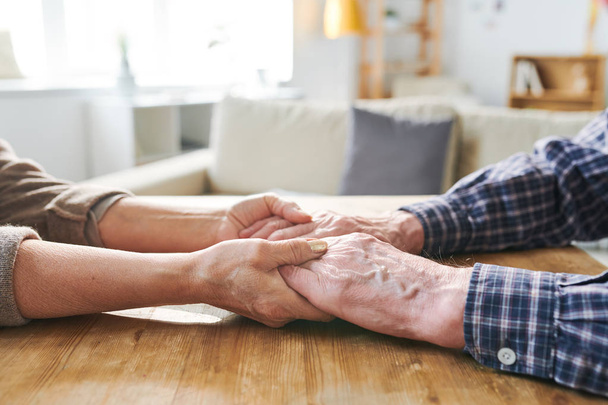 Due anziani che si tengono per mano seduti al tavolo di legno ed esprimono amore, cura e sostegno
 - Foto, immagini