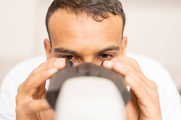 Nahaufnahme eines fokussierten jungen arabischen Arztes, der Augenlinsen justiert, während er Mikroskop benutzt und Bakterien untersucht - Foto, Bild