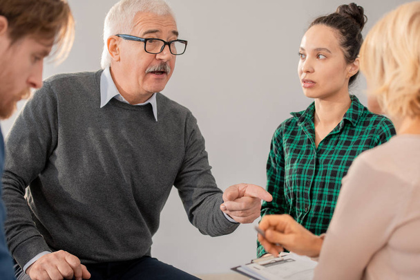 Ανώτερος άνθρωπος σε γυαλιά που δείχνουν ψυχοθεραπεύτρια μεταξύ των συντρόφων ενώ εξηγούν το πρόβλημά του κατά τη συνεδρία - Φωτογραφία, εικόνα