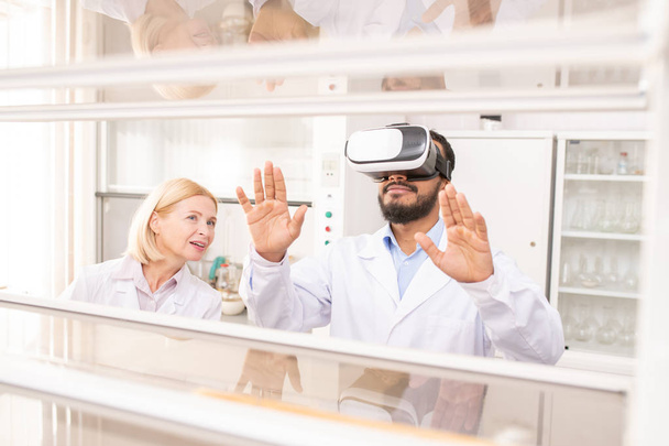 Content curious Arabian bearded laboratory worker in white coat molding shape of gene while using virtual reality simulator - Foto, Bild