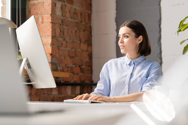 Jonge kantoormedewerker drukken toetsen van de computer toetsenbord, terwijl het kijken naar het scherm en het analyseren van online informatie - Foto, afbeelding