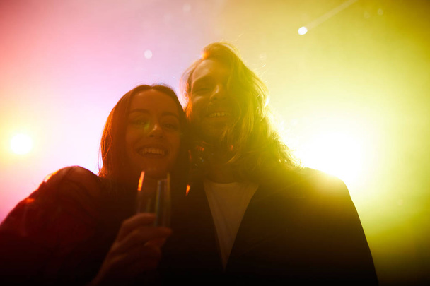 Portrét šťastného vzrušeného mladého páru stojícího v barevných světlech a s objímám pohromadě - Fotografie, Obrázek