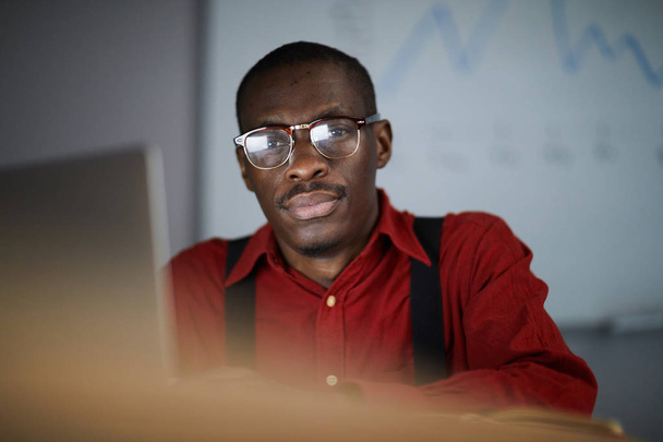 Portrét moderního afrického podnikatele, který se dívá na kameru při práci v tmavé kanceláři, kopírovací prostor - Fotografie, Obrázek