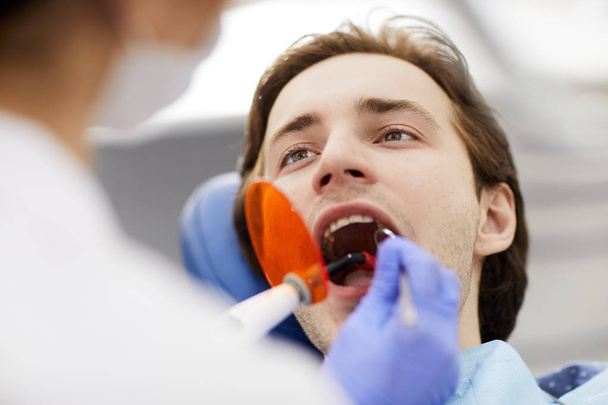 Unerkennbarer Zahnarzt, der Laser-Zahnaufhellung an einem Mann durchführt, der mit offenem Mund im Zahnarztstuhl sitzt, Kopierraum - Foto, Bild