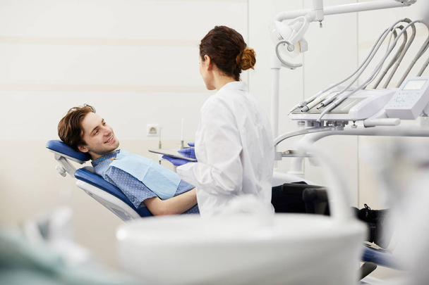 Πορτραίτο του χαμογελαστή νεαρού άντρα που κάθεται στην καρέκλα οδοντιάτρων κατά τη διάρκεια της διαβούλευσης, αντιγράψτε χώρο - Φωτογραφία, εικόνα