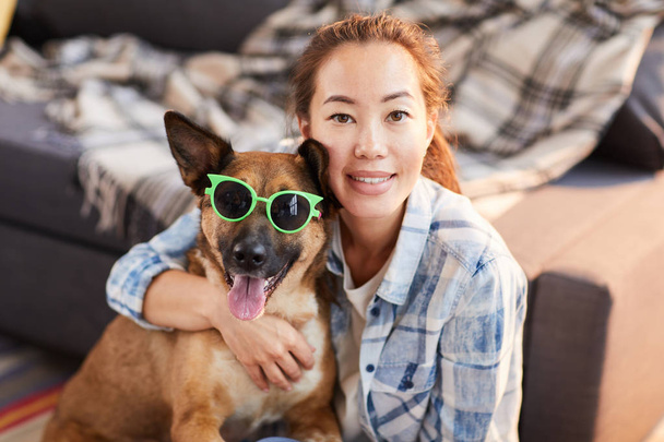 Retrato de mulher asiática sorridente posando com cão de estimação vestindo óculos de sol e olhando para a câmera, espaço de cópia
 - Foto, Imagem