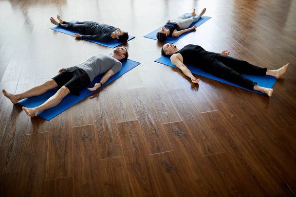 Group of relaxed young people lying on mats in circle and doing savasana while napping at end of yoga practice - Foto, Imagem