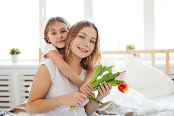 Waist up portrait of cute little girl embracing mother on Mothers day, both posing looking at camera, copy space - Photo, Image