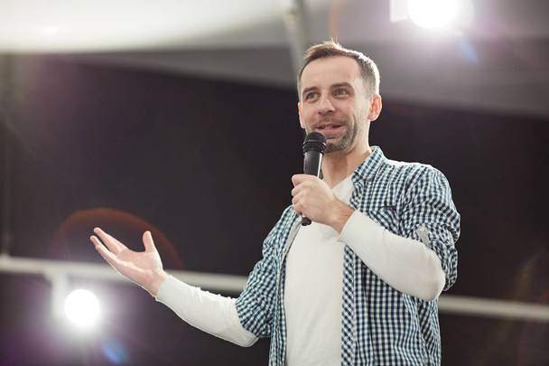 Waist up portrait of mature man giving speech standing on stage in spotlight and speaking to microphone, copy space - Photo, Image